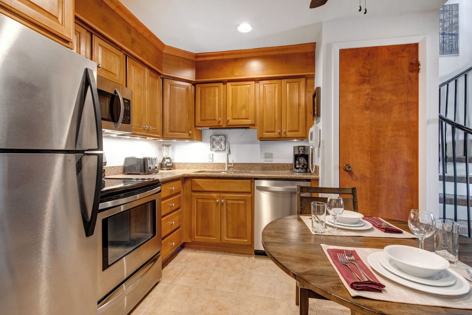Medium toned wood cabinets with stainless steel appliances, under cabinet lighting and white walls.