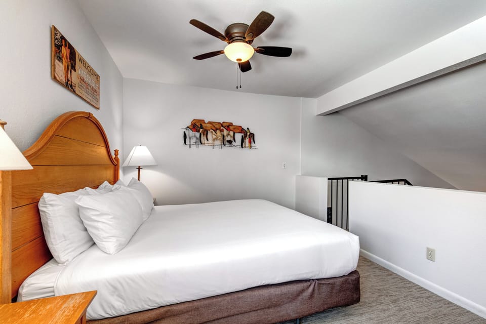 Snow Flower 31's loft with a king size bed with crisp white linens, night stands with lamps, stair entry, and picture on wall.