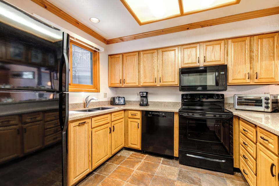 Snow Flower 43's kitchen with black appliances, oak cabinets, large overhead lighting, and tile floor.