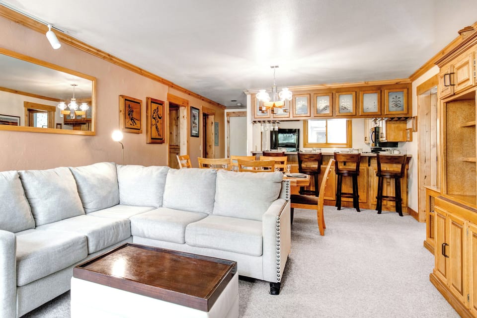 Snow Flower 43's living room looks into the dining area and kitchen and has cream colored carpet and wood trim.