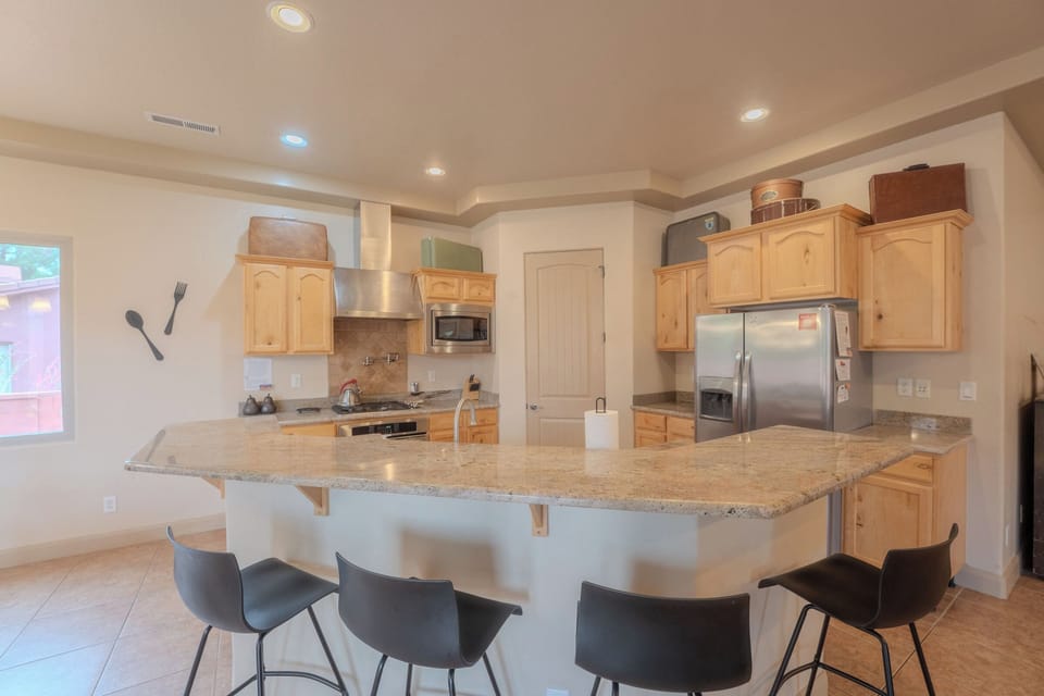 Spacious kitchen with curved granite island seating for four, stainless appliances, and light wood cabinetry.