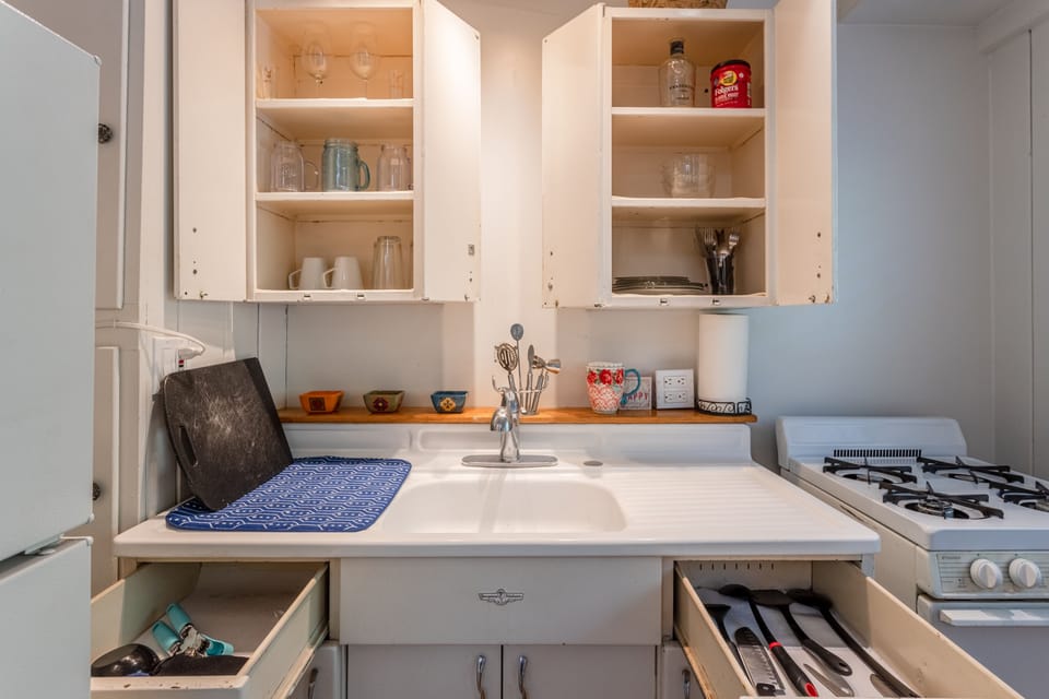 Kitchen stocked up with glassware, oven and stove top and fridge.