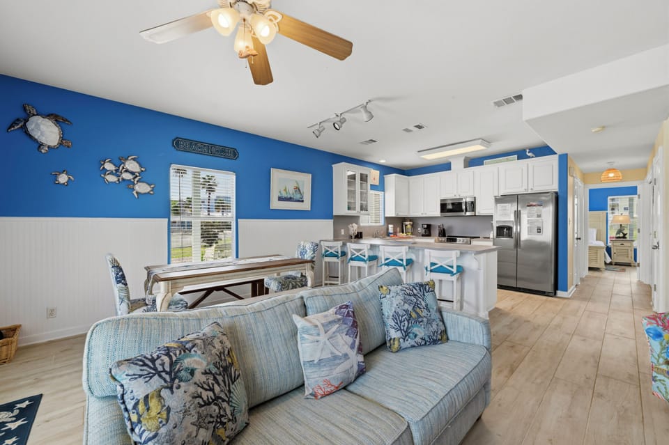 Picture yourself relaxing on the sofa with coastal breezes and beach-themed decor all around. Your open kitchen stands ready for meals, while sea turtle art and ocean-blue walls set the perfect seaside mood.