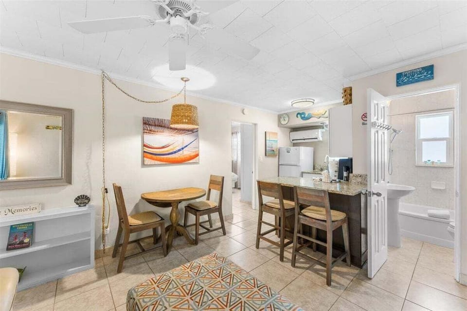 Open living and dining area with round table, granite breakfast bar with seating, AC unit, and cheerful coastal touches throughout.