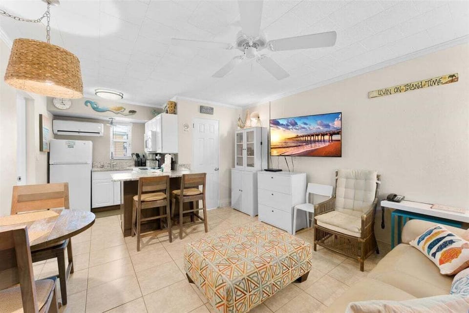 Open living and dining area with round table, granite breakfast bar with seating, AC unit, and cheerful coastal touches throughout.