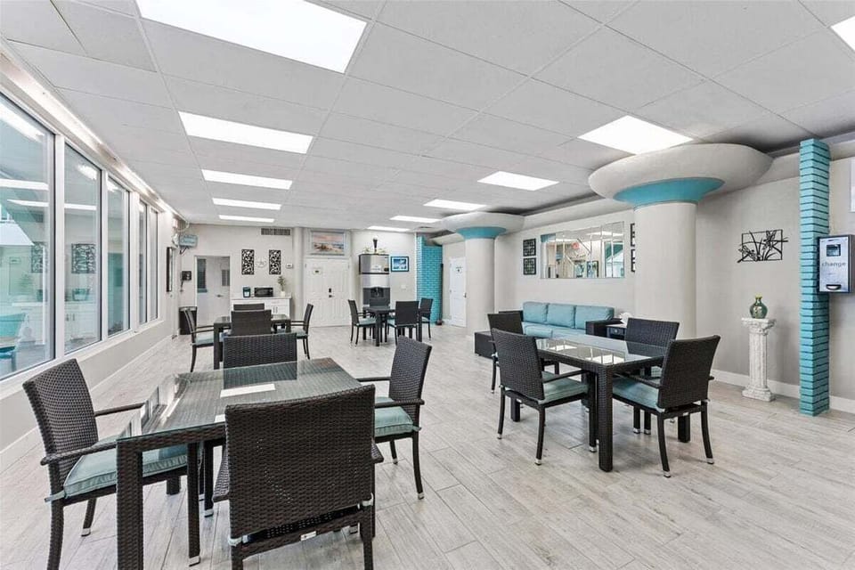 Clubhouse lounge with stylish seating, smart TV, and floor-to-ceiling windows overlooking the tropical courtyard — perfect for games, socializing, or relaxing.