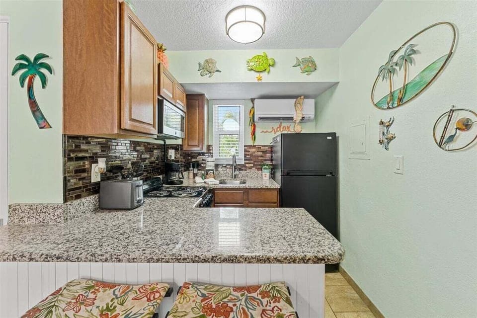 Fully equipped kitchen with granite counters, mosaic tile backsplash, stove, microwave, and fridge — plus a breakfast bar for casual dining with a side of tropical charm.