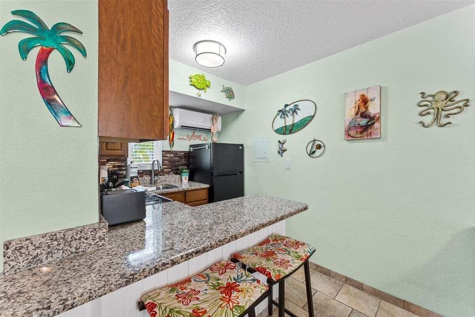 Fully equipped kitchen with granite counters, mosaic tile backsplash, stove, microwave, and fridge — plus a breakfast bar for casual dining with a side of tropical charm.