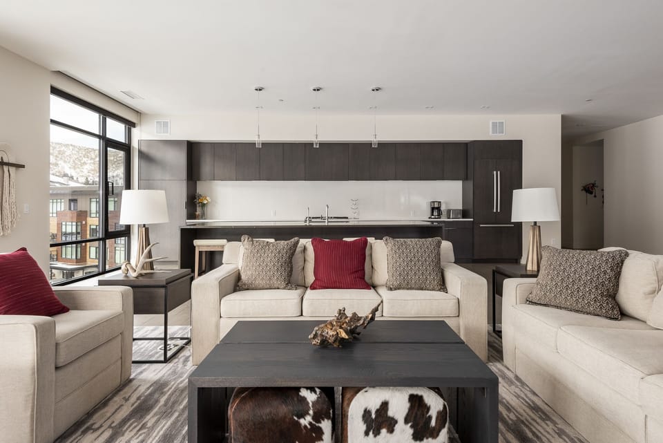 Living room with two white couches, one is a sofa sleeper, wooden coffee table with cowhide cube poufs