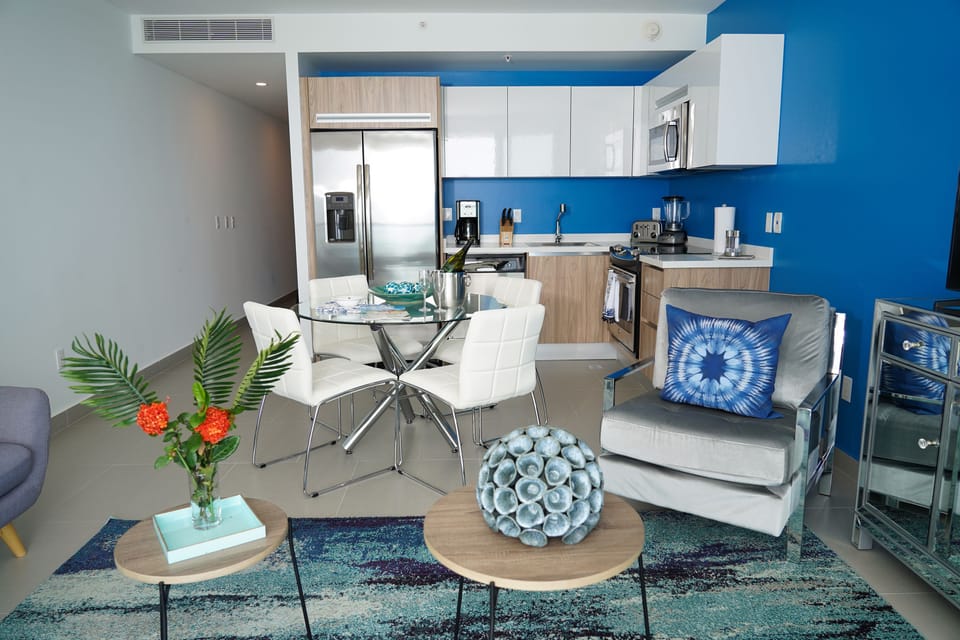 Step into your bright, modern space where the vibrant blue kitchen anchors stylish open-plan living. Cook with stainless steel appliances, dine under soft ambient lighting, and unwind on sleek furnishings—all designed for your comfort.