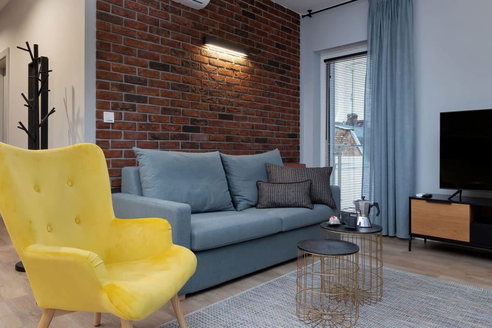 A contemporary living room with a gray sofa, yellow armchair, gray carpet, and exposed brick wall.