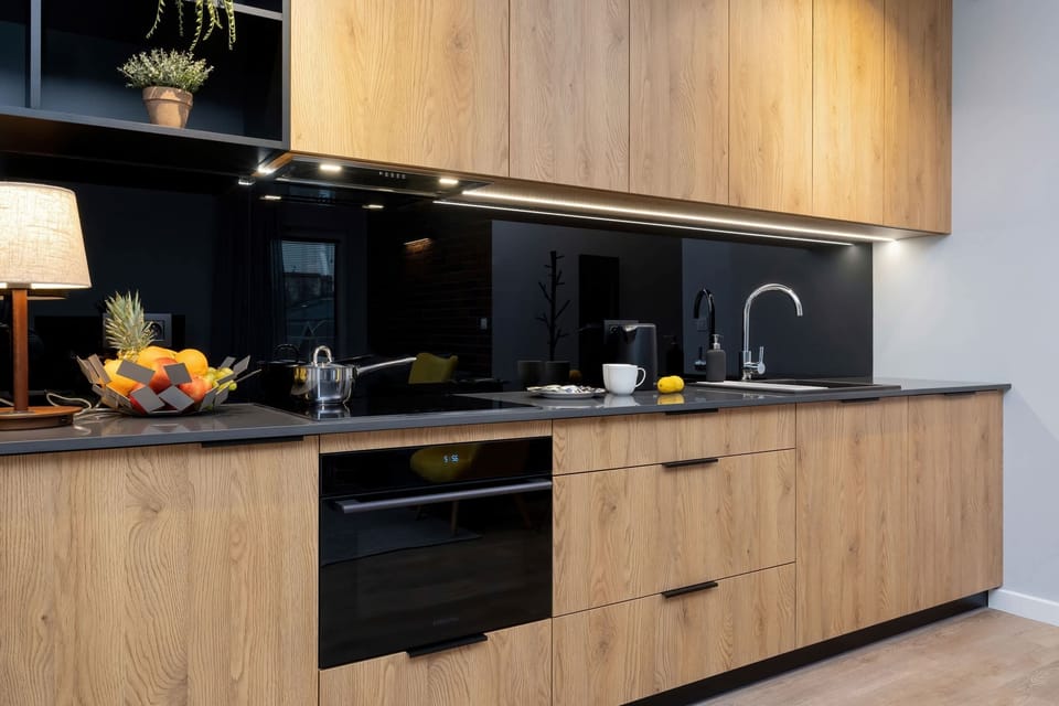 Modern fully equipped kitchen with appliances such as dishwasher, oven, fridge and induction hob. The cabinets are wood coloured and match to the black worktop.