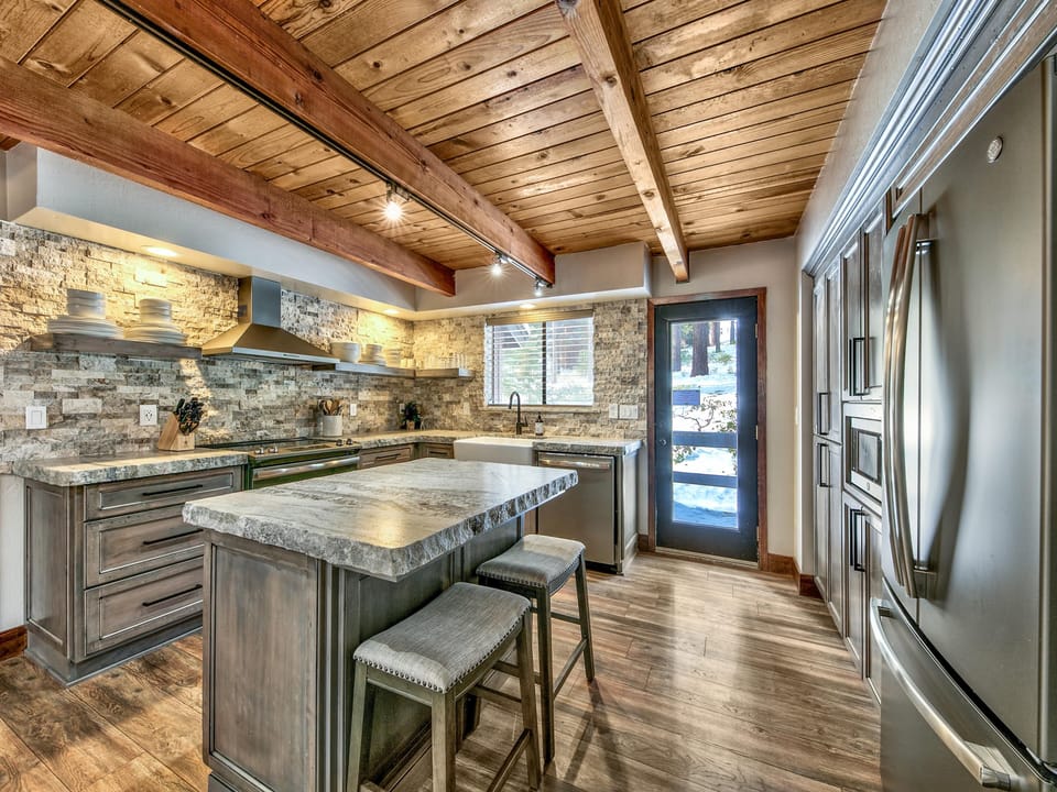 Kitchen with rough-edge stone countertops, gray wood cabinets, stainless steel appliances, and wood-plank ceiling.