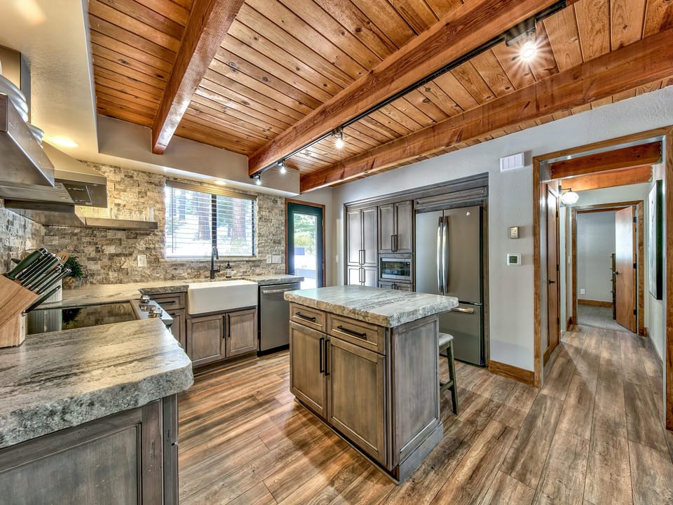 Kitchen features a stone tile backsplash, farmhouse sink under a window, central island, and wood-plank floors.