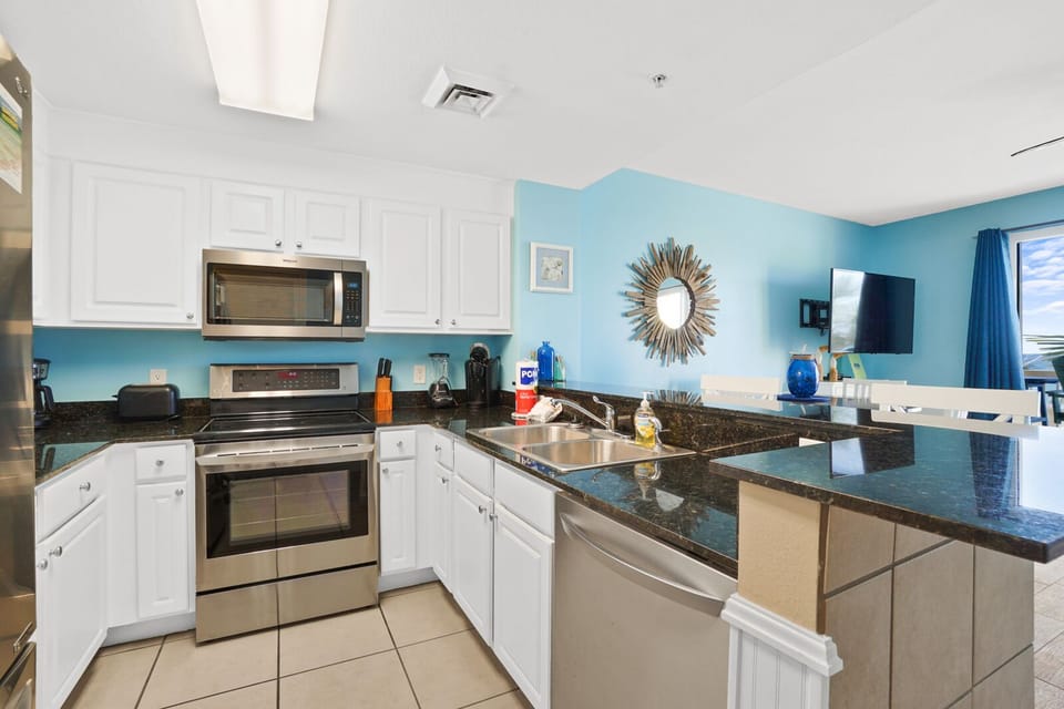 Your fully equipped kitchen awaits with granite counters, stainless appliances, and coastal blue walls creating the perfect space for preparing memorable meals.