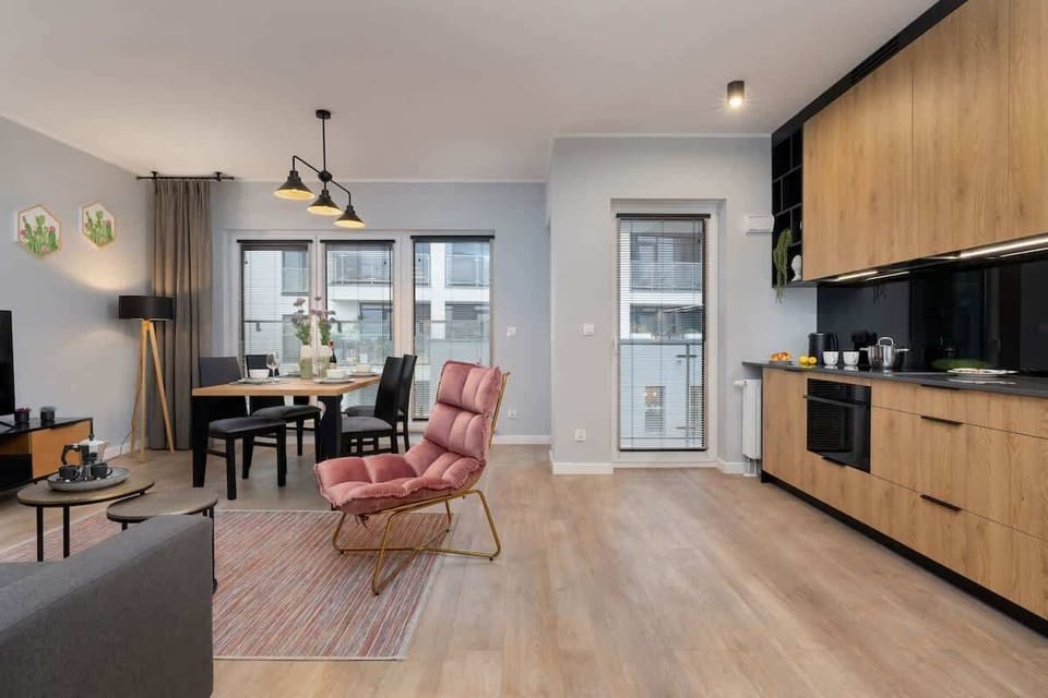  A spacious living room with a brick wall, a pink armchair, a gray sofa, a coffee table, and an open view into the dining and kitchen area.