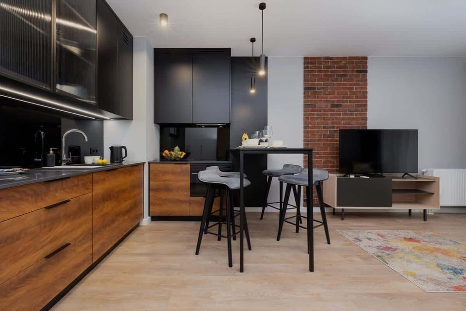 Functional kitchen with imitation wood cabinet fronts and upper black cabinets. A high countertop with bar chairs offers space for dining.