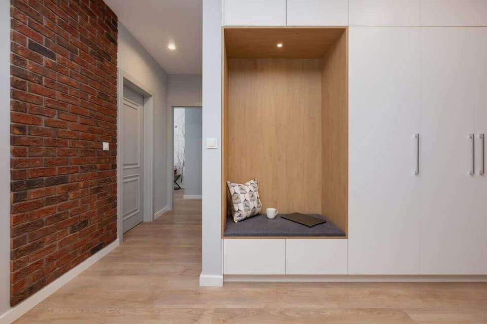Bright hallway with a brick wall and large wardrobe in which an alcove with a seat and decorative cushion has been arranged.