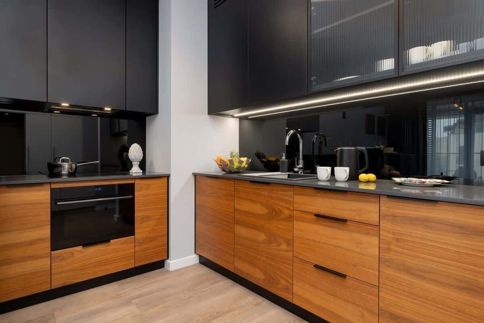 Modern fully equipped kitchen with appliances such as dishwasher, oven, fridge and induction hob. The lower cabinets are wood coloured and the upper cabinets are black to match the black worktop.