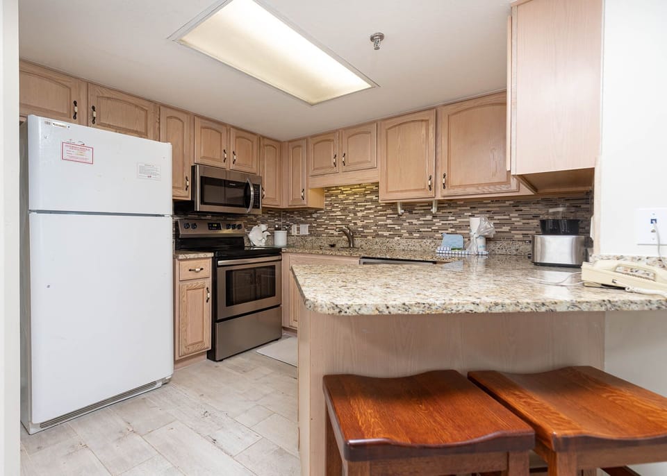 Kitchen featuring light wood cabinetry, granite countertops, and stainless appliances, with two wooden stools at the bar