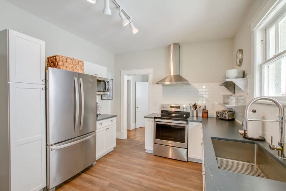 Kitchen with white cabinets, stainless steel refrigerator, gas range with hood, and hardwood floors