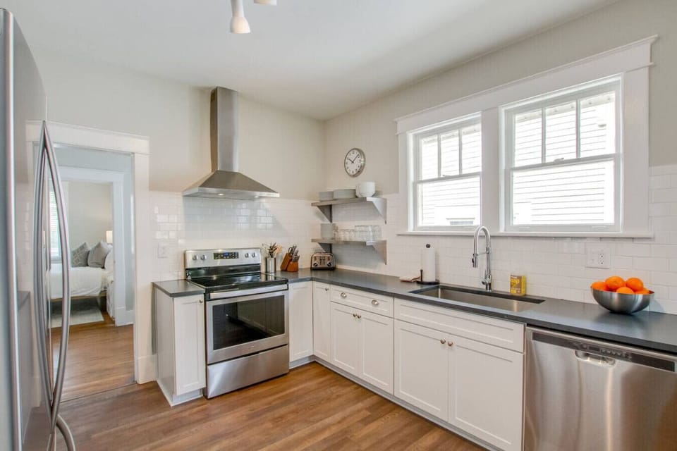 Kitchen from alternate angle showing range with hood, white cabinets, and large windows