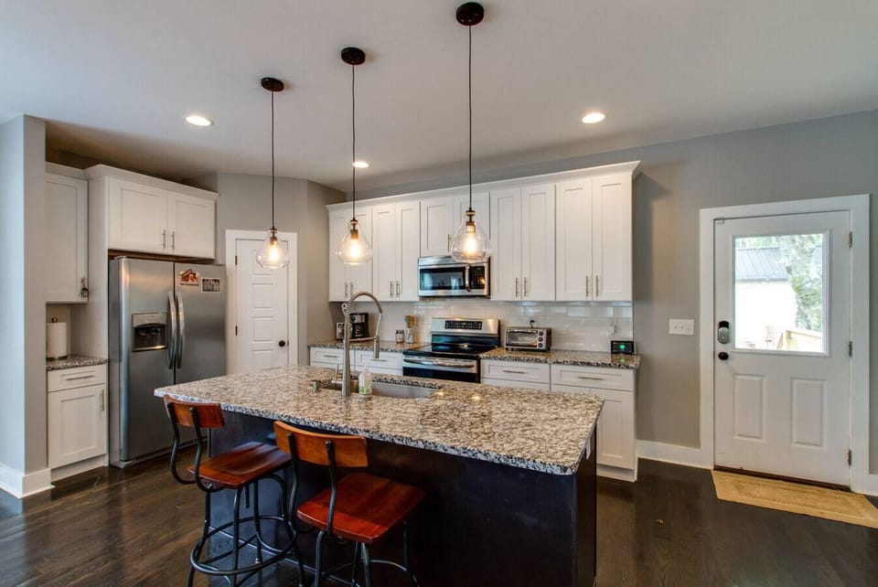 Kitchen with granite island and bar stools, white cabinets, and stainless steel appliances