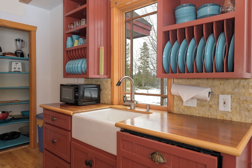 Your charming kitchen features warm wood cabinetry, a farmhouse sink, and thoughtfully organized dishes—perfect for preparing home-cooked meals with snowy mountain views.