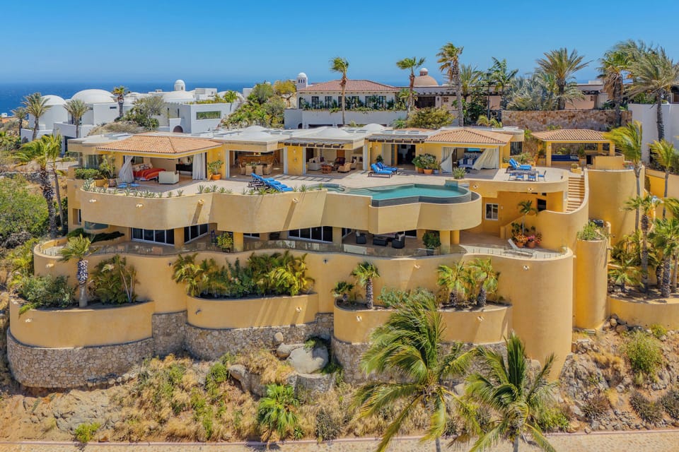Stunning multi-level villa with curved architecture overlooks tropical coastline, featuring terraced gardens and azure pool amid swaying palms.