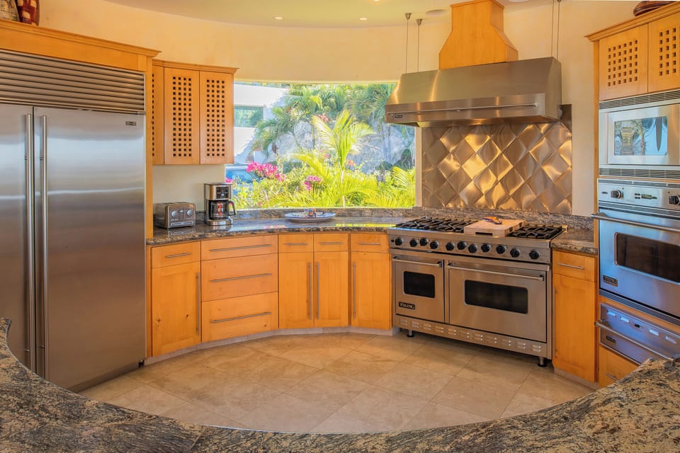 Your gourmet kitchen awaits with professional-grade appliances, granite counters, and tropical garden views through the window.