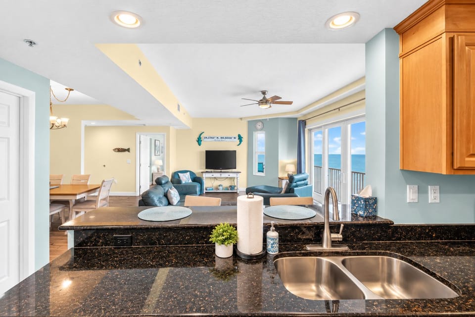 Seamlessly designed coastal kitchen and living space with granite counters, stainless sink, and stunning ocean views through expansive doors.