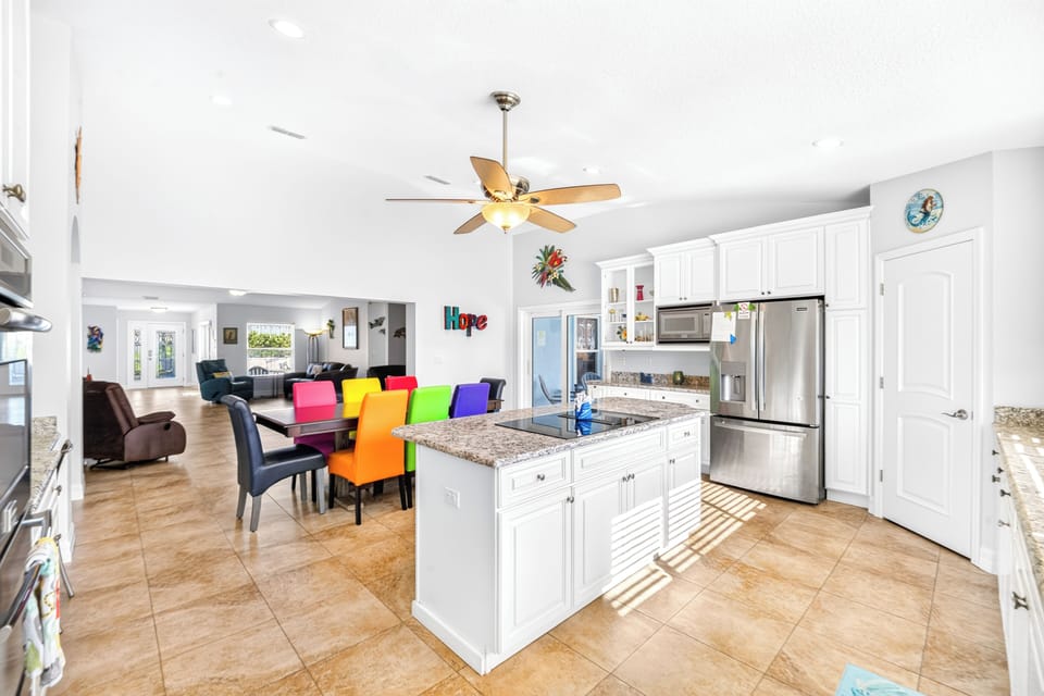Bright open-concept space with white cabinetry, granite counters, and rainbow dining chairs that add a cheerful pop to your group gatherings and meal prep.