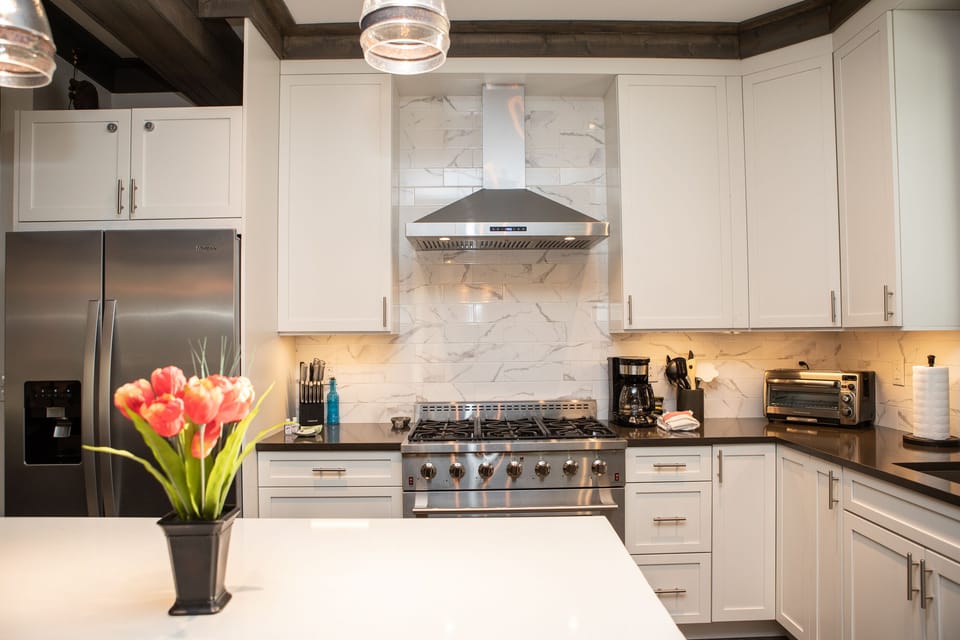 A modern kitchen with white cabinets, stainless steel appliances, a marble backsplash, and a vase of red flowers on the island countertop.