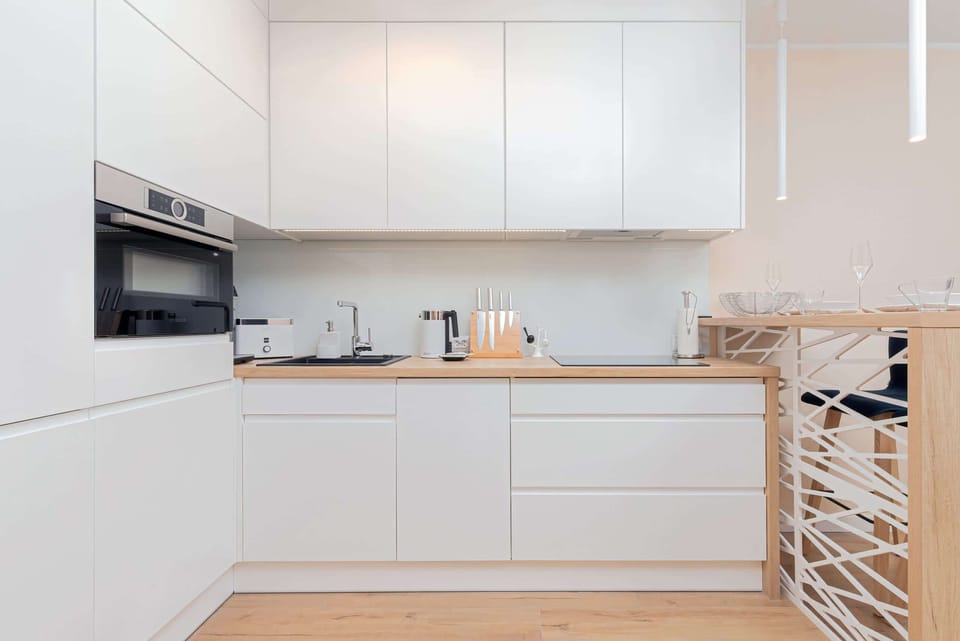 A sleek, white kitchen with minimalist cabinetry and a cozy dining area featuring light wood accents and subtle decorative touches.
