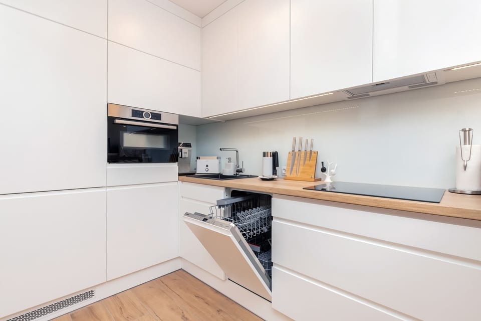 A sleek, white kitchen with minimalist cabinetry and a cozy dining area featuring light wood accents and subtle decorative touches.