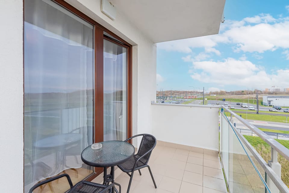 A balcony with a small table and chairs, offering a great view of the surroundings, including greenery and neighboring buildings.