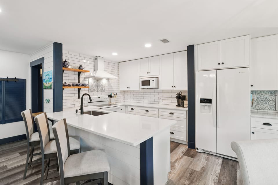 Your fully-equipped kitchen features sleek white cabinetry, modern appliances, and a spacious island—perfect for preparing meals and gathering with loved ones during your stay.