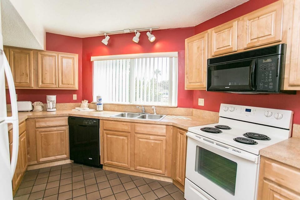 - Spacious kitchen with stove, oven, microwave, and cabinets for easy meal preparation
- Red accent walls pair beautifully with wood cabinetry for a bold warm setting
- Large window brightens the space making it cheerful and functional