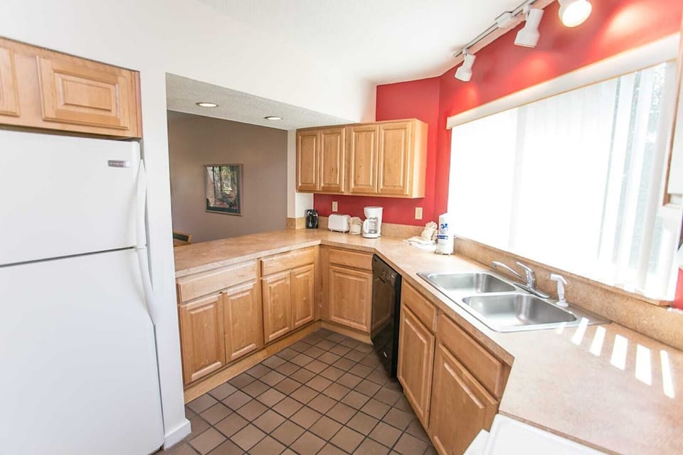 - U shaped kitchen design with dual sinks and wide countertops for convenience
- White refrigerator and coffee maker station add to guest friendly setup
- Rich red walls contrast beautifully with light wood finishes throughout