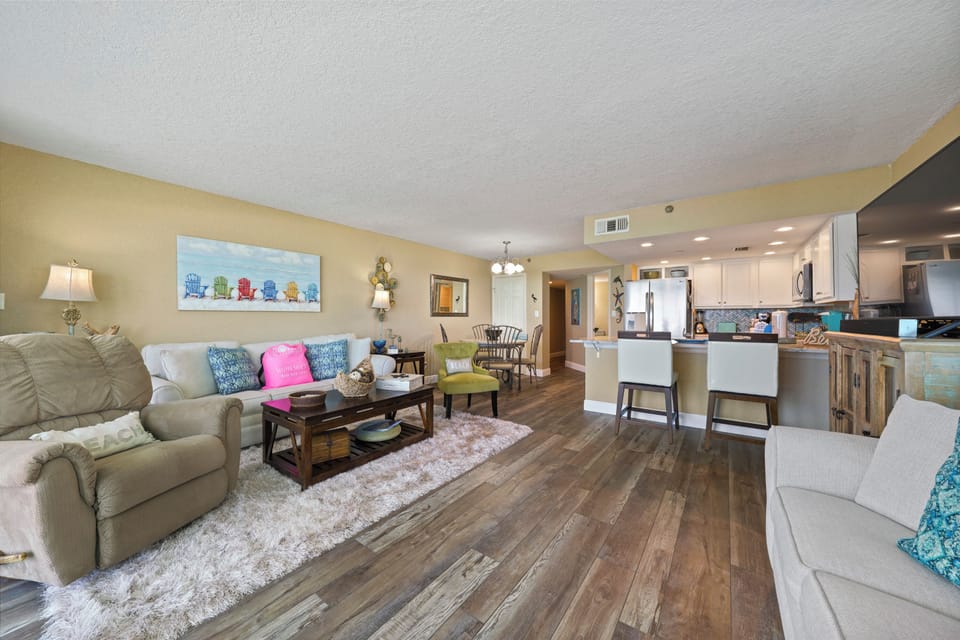 Cabana Club 101 offers a living room that embodies beachside relaxation with two sleeper sofas, natural light pouring through corner windows, and sweeping views of Destin's Gulf waters