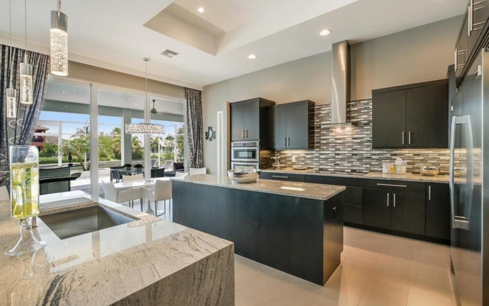 Kitchen featuring dark cabinetry, granite island with bar seating, stainless appliances, and decorative tile backsplash