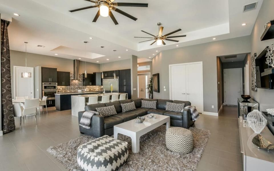 Sleek open-concept living room with dark sectional sofa, modern coffee table, and kitchen visible in the background