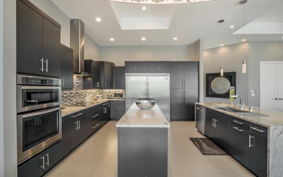 Kitchen from alternate angle showcasing dark cabinetry, stainless range with hood, pendant lighting, and granite counters