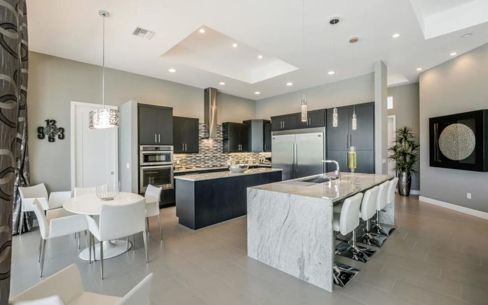 Gourmet kitchen with dark cabinetry, large white marble island with bar stools, and stainless steel appliances
