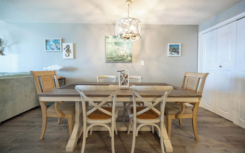 Dining area featuring a large rustic table, six stylish chairs, and coastal artwork, perfect for family meals and gatherings