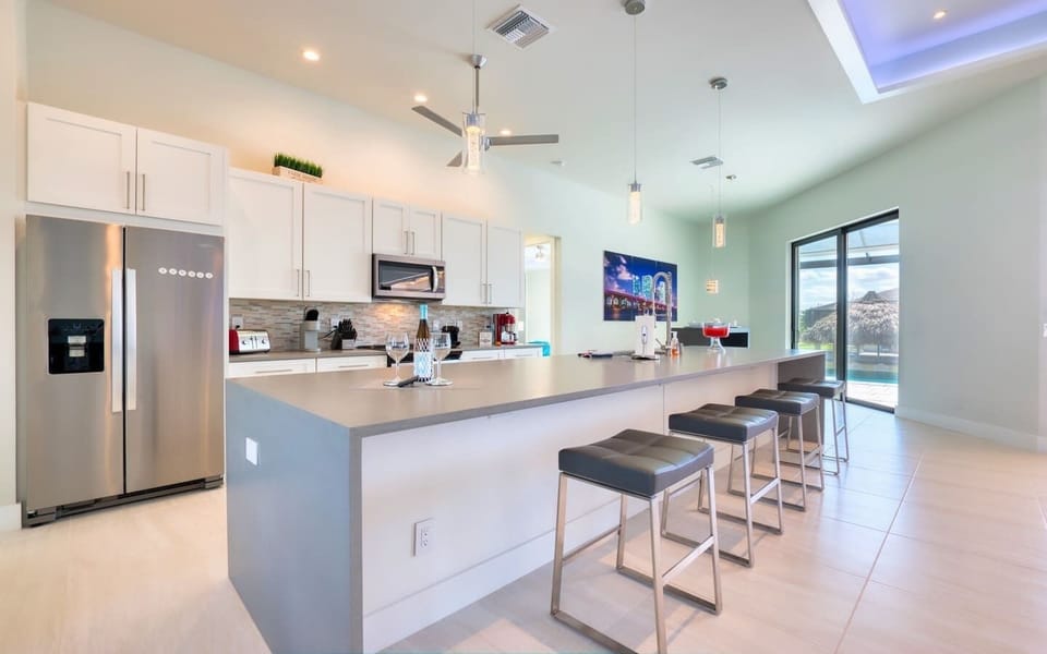 Open kitchen with a large island, bar seating, pendant lights, stainless steel appliances, and modern cabinetry