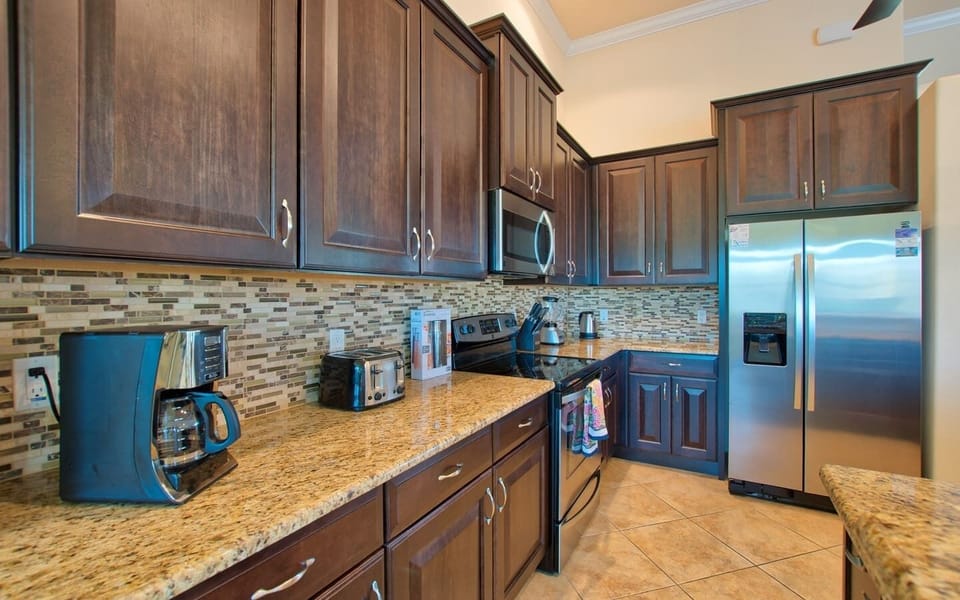 Kitchen detail showing stainless steel refrigerator, microwave, and dark wood cabinetry with granite countertops