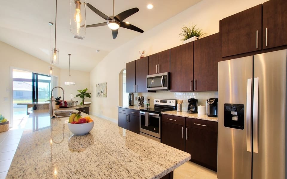 Kitchen counter with a fruit bowl, stainless steel appliances, and dark wood cabinetry with granite countertops