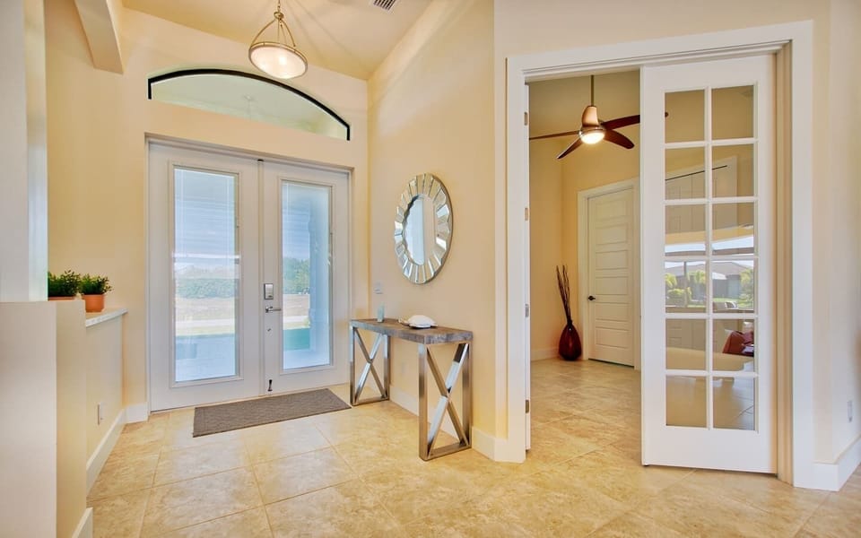 Formal entryway with a decorative console table, round wall mirror, and double front doors