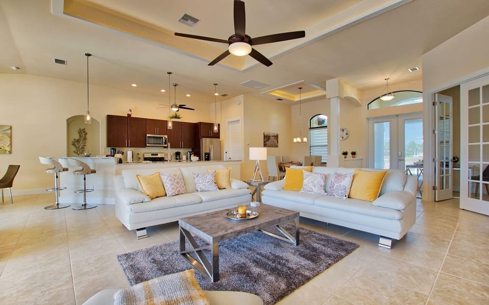 Open-concept living room and kitchen showing the sofa, kitchen island, and natural light from large windows